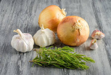 Photo for A closeup of onions and garlic together with rosemary leaves on wooden surface - Royalty Free Image