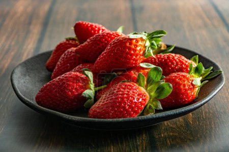 Foto de Un primer plano de fresas frescas y deliciosas en un plato oscuro - Imagen libre de derechos