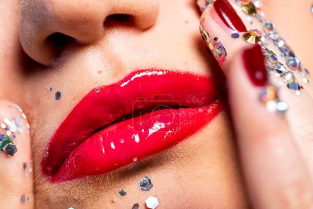 Photo for Close-up of beautiful young woman with bright red glossy lipstick touching face with shiny glitters - Royalty Free Image