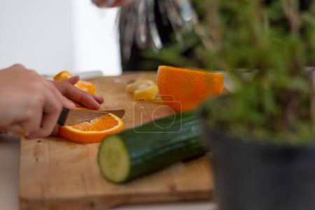 Téléchargez les photos : Gros plan d'un chef coupant orange et concombre sur une planche à découper dans la cuisine - en image libre de droit