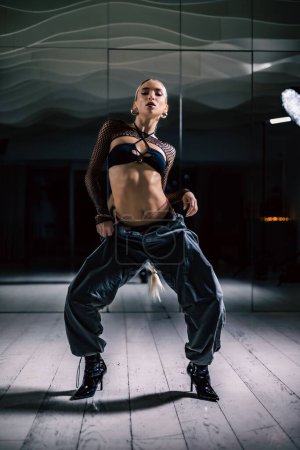 Eine vertikale Aufnahme einer schönen Tänzerin posiert in Mesh-Overlay Crop Top in schwarzen und sackartigen Hosen