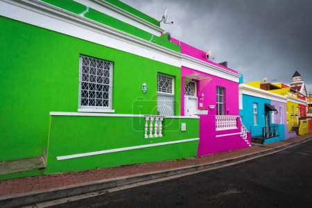 A row of colorful houses painted in vibrant green, pink and blue on a street in Africa under a cloudy sky