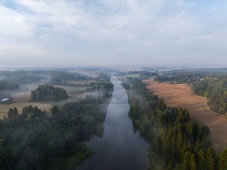 Photo for An aerial view of a foggy forest and calm river in the countryside during sunrise - Royalty Free Image