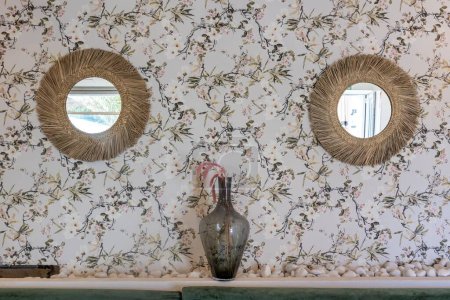 Foto de Un jarrón puesto en medio de dos espejos redondos colgando de una pared estampada con flores - Imagen libre de derechos