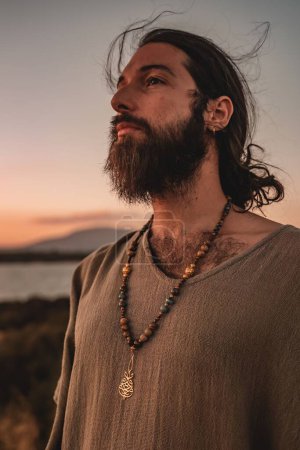 Téléchargez les photos : Un gros plan vertical d'un homme caucasien sexy avec des poils du visage posant sur une plage au coucher du soleil - en image libre de droit