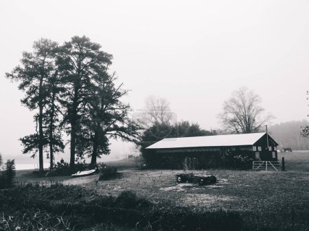 Foto de Un hermoso tiro a escala de grises de un granero con su patio en un día de niebla - Imagen libre de derechos