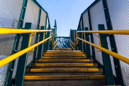 Téléchargez les photos : Plan à angle bas d'un escalier avec des mains courantes jaunes et une clôture verte des deux côtés - en image libre de droit