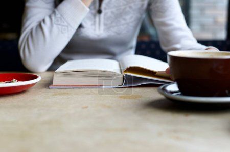 Foto de Una mujer sentada en una mesa leyendo un libro con café y comida cerca - Imagen libre de derechos