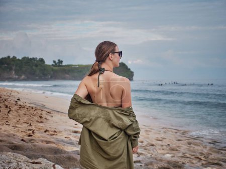 Foto de Una hermosa mujer caucásica en traje de baño posando en la playa de arena con el mar azul en el fondo - Imagen libre de derechos