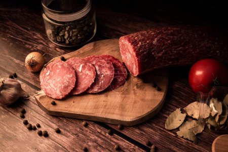 Photo for A closeup of sliced smoked meat on a wooden board next to fresh organic ingredients - Royalty Free Image