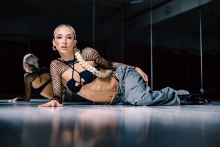 Photo for A beautiful female dancer in a mesh overlay crop top in black and baggy pants posing on the floor - Royalty Free Image