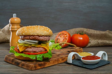 Foto de Primer plano de una deliciosa hamburguesa entera en una tabla de madera y salsas - Imagen libre de derechos