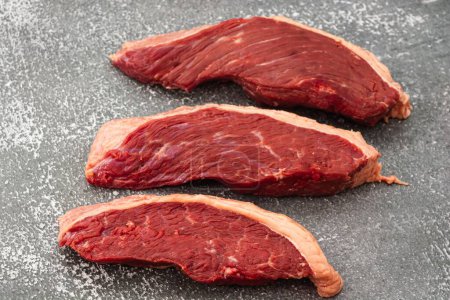 A closeup shot of three raw picanha steaks on a stone table