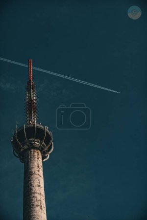 Téléchargez les photos : Un plan vertical à faible angle d'une tour de télévision et une traînée dans le ciel bleu sans nuages - en image libre de droit