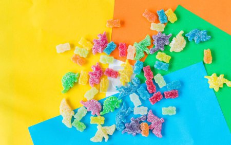 Photo for A flat lay of colorful gummy candies in the shape of a dinosaur and a bear covered in sour powder on colorful background - Royalty Free Image