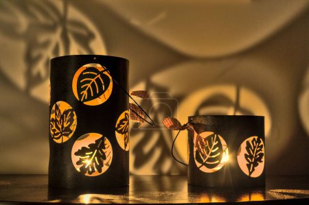 Photo for The two lit candles of different sizes with leaf-shaped cutouts in a room - Royalty Free Image
