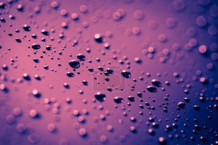 Foto de Un primer plano de gotas de lluvia en una ventana de coche con un fondo púrpura - Imagen libre de derechos