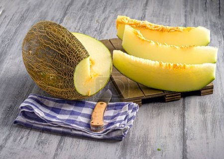 Photo for A closeup of almost whole melon and melon slices with knife on a wooden board - Royalty Free Image