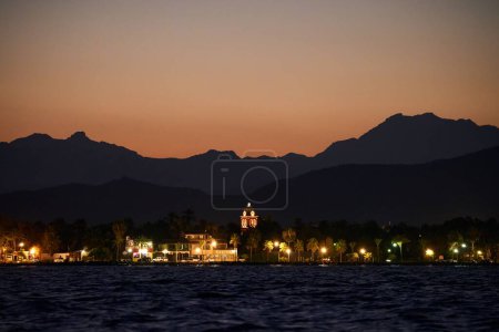 Una vista nocturna de la ciudad con su paseo marítimo, y siluetas de montaña en el fondo