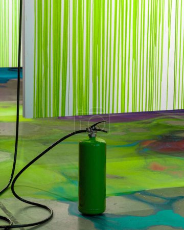 Photo for A vertical shot of a green fire extinguisher on a colorful floor with green and white wall behind it - Royalty Free Image