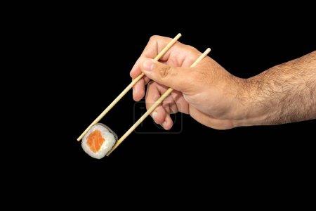 Téléchargez les photos : La main masculine tenant un rouleau de sushi avec des baguettes, isolé sur le fond noir. - en image libre de droit