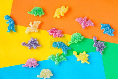 Téléchargez les photos : Une couche plate de bonbons gommeux colorés en forme de dinosaure et un ours recouvert de poudre sure sur fond coloré - en image libre de droit