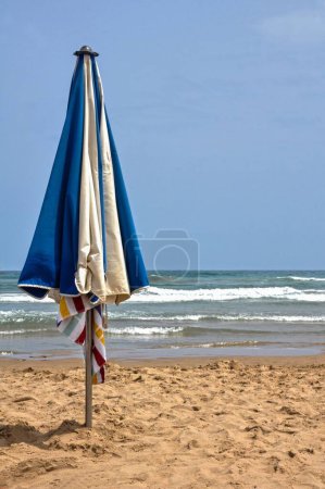 Photo for A vertical shot of a blue and white beach umbrella planted in the sand in Gandia, Valencia, Spain - Royalty Free Image