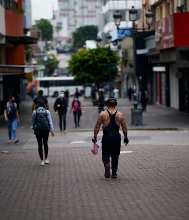 Foto de Un hombre musculoso y tatuado con auriculares caminando por las concurridas calles de San José durante la pandemia - Imagen libre de derechos