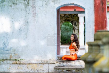 Téléchargez les photos : Une jeune femme brune en tenue de sport orange pratiquant le yoga dans un parc par une journée ensoleillée - en image libre de droit