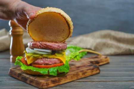 Foto de Primer plano de las manos de una mujer abriendo el bollo de un bollo de hamburguesa completo con dos trozos de carne en una tabla de madera - Imagen libre de derechos