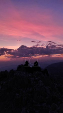 Téléchargez les photos : Un plan vertical d'un ciel rose envoûtant au coucher du soleil sur la silhouette d'un couple assis sur la colline rocheuse - en image libre de droit