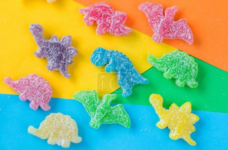 Photo for A flat lay of colorful gummy candies in the shape of a dinosaur and a bear covered in sour powder on colorful background - Royalty Free Image