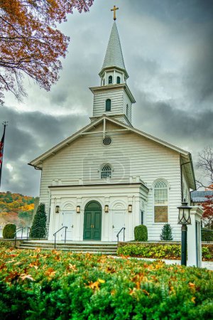 Photo for An old white church with a steeple surrounded by foliage and trees - Royalty Free Image