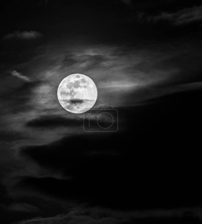 Téléchargez les photos : Un cliché en niveaux de gris de la pleine lune dans le ciel nuageux sombre - en image libre de droit
