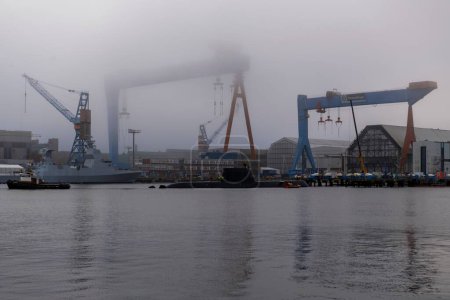 Foto de Barcos y grúas en el mar en el astillero contra el cielo en la ciudad durante el tiempo brumoso - Imagen libre de derechos