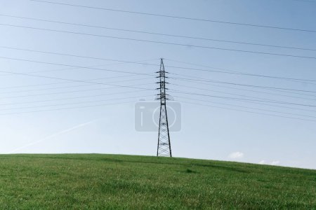 Foto de Torres de transmisión de energía en el paisaje. postes eléctricos de alta tensión con líneas de cable en el campo verde bajo el cielo soleado azul claro. - Imagen libre de derechos