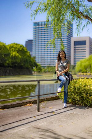 Photo for A vertical shot of an East Asian female leaned on the bridge railing  in the park - Royalty Free Image