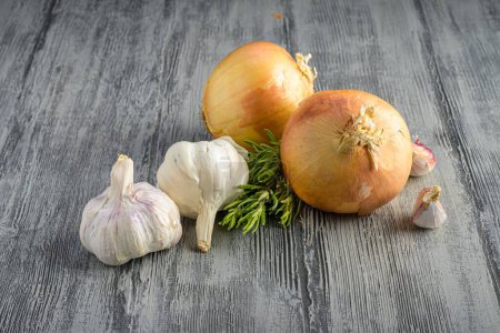 Photo for A beautiful closeup of two garlic and two onions with rosemary leaves on a gray wooden surface - Royalty Free Image