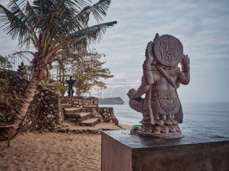 Téléchargez les photos : Statue d'une créature mythologique placée sur une plage avec des palmiers et la mer en arrière-plan - en image libre de droit