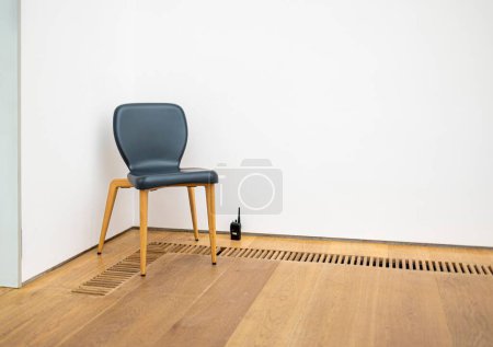 Téléchargez les photos : Une chaise et un talkie-walkie contre un mur blanc sur un plancher de bois. - en image libre de droit
