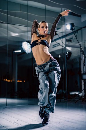 Eine vertikale Aufnahme einer schönen Tänzerin posiert in Mesh-Overlay Crop Top in schwarzen und sackartigen Hosen