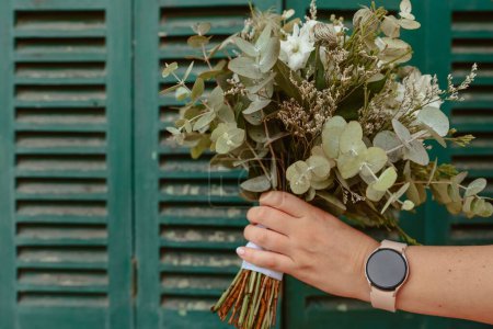 Foto de Una mano femenina con un reloj inteligente sosteniendo un ramo floral cerca de una vieja pared de madera - Imagen libre de derechos