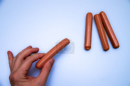 Photo for A closeup of a person's hand next to raw sausages isolated on a blue background - Royalty Free Image
