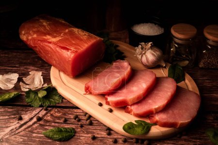 Photo for A closeup of delicious sliced smoked meat on a wooden board next to fresh organic ingredients - Royalty Free Image