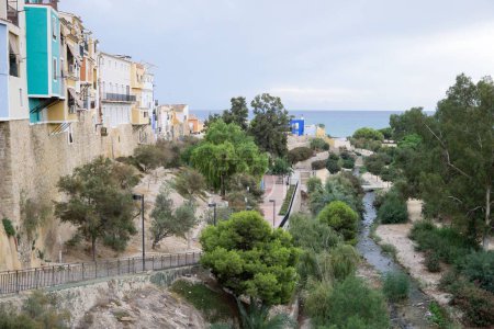 Téléchargez les photos : Une petite rivière à Alicante entre de beaux bâtiments et des arbres avec la mer en arrière-plan, Espagne - en image libre de droit