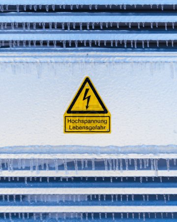 Foto de ¡Un plano vertical de Atención! Señal de alto voltaje en alemán sobre superficie congelada - Imagen libre de derechos