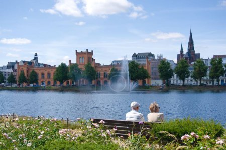 Photo for An old couple sits at the lake on a bench and enjoys the sun in Schwerin, Germany - Royalty Free Image