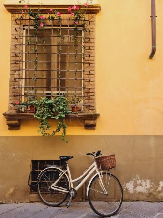 Téléchargez les photos : Une bicyclette blanche garée à côté d'un bâtiment jaune sous une fenêtre clôturée - en image libre de droit
