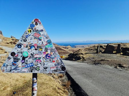 Foto de Un primer plano de una señal de tráfico cubierta con pegatinas cerca de un camino rural vacío. Skye, Escocia, Reino Unido. - Imagen libre de derechos