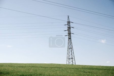 Foto de Torres de transmisión de energía en el paisaje. postes eléctricos de alta tensión con líneas de cable en el campo verde bajo el cielo soleado azul claro. - Imagen libre de derechos